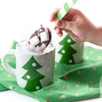 small hand holding a chocolate stirring spoon dunking it in warm milk.