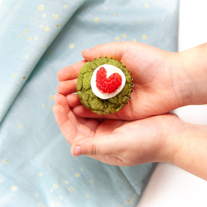 Two small toddler hands holding a mini green grinch muffin.