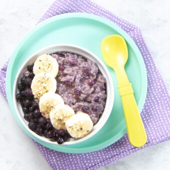Bowl filled with blueberry oatmeal with slices of banana and frozen blueberries on top.