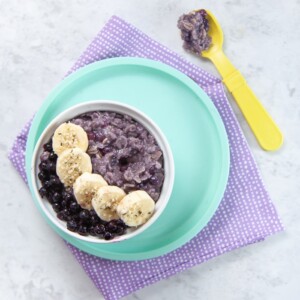 Bowl filled with blueberry oatmeal with slices of banana and frozen blueberries on top.