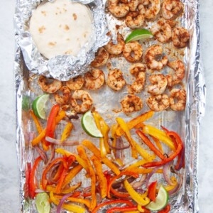 Sheet pan with cooked shrimp tacos and tortillas on top.