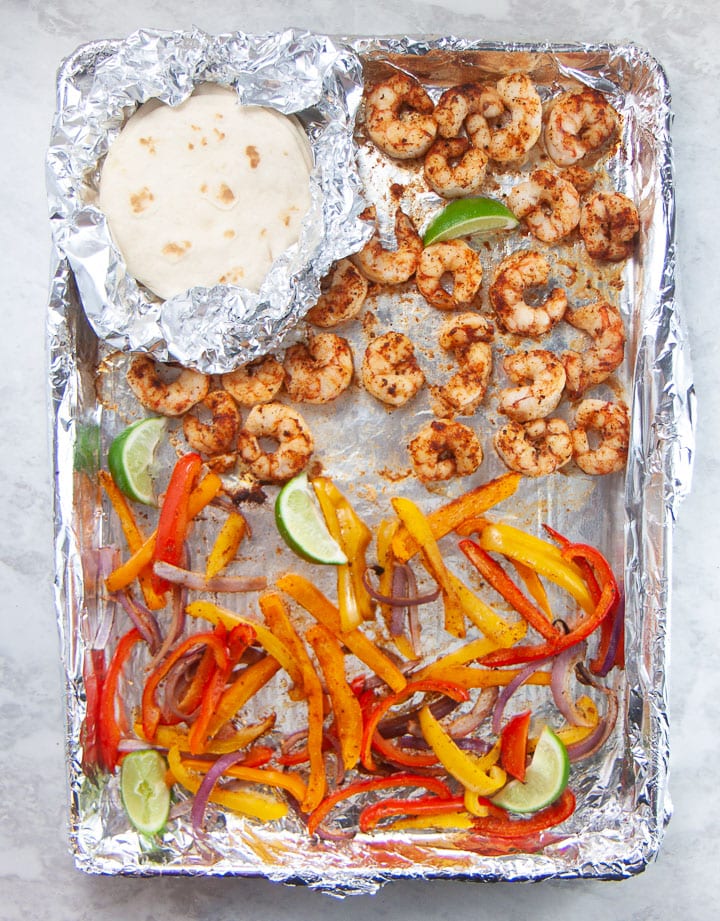 Sheet pan with cooked shrimp tacos and tortillas on top.
