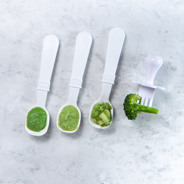 Lineup of spoon and a fork with different stages of baby food on it.