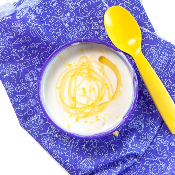 Small purple kids bowl with yogurt honey and lemon inside against a purple kids napkin.