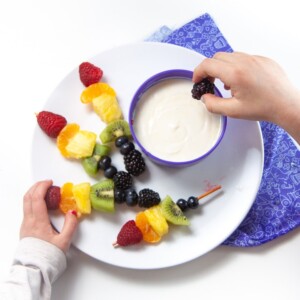 rainbow skewers on a plate with a bowl of yogurt dip.
