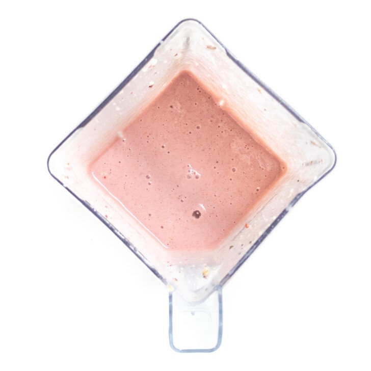Clear blender with a strawberry smoothie sitting on a white counertop.