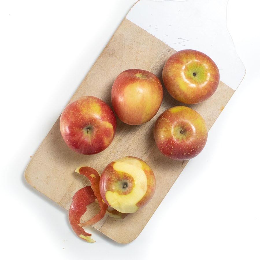 Wood cutting board with six apples on top one peeled.