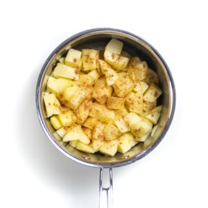 Silver sauce pan on a white background with raw chopped apples and sprinkled with cinnamon.