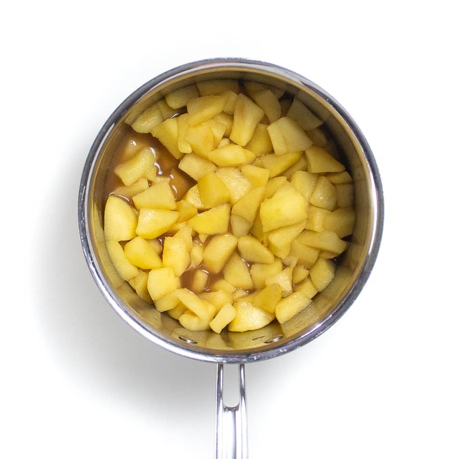 Silver sauce pan on a white background with cooked tender chunks of apples.