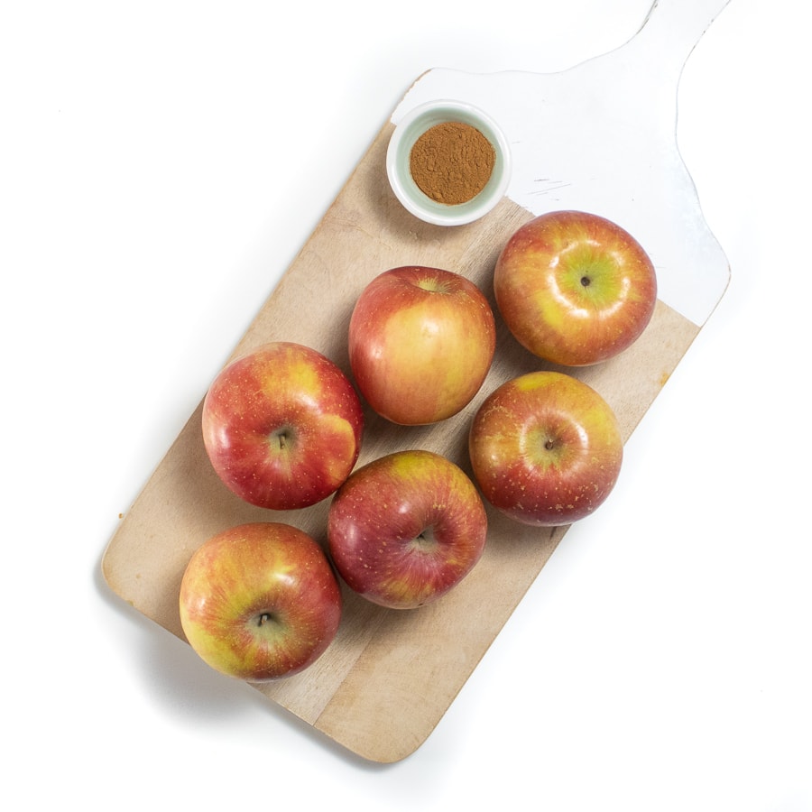 Wooden cutting board with six apples and a small white bowl of cinnamon.