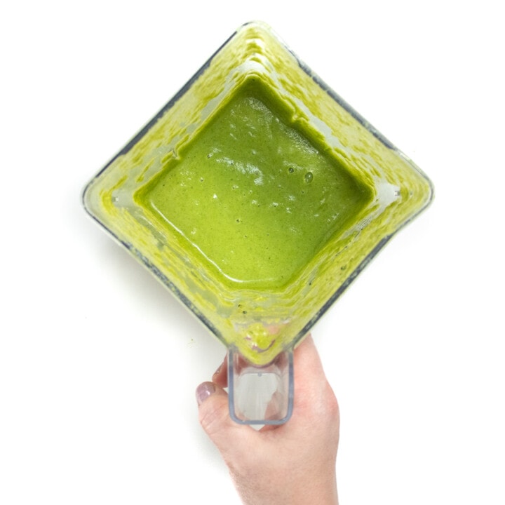 Blender with pureed broccoli for baby with a hand holding onto the handle.