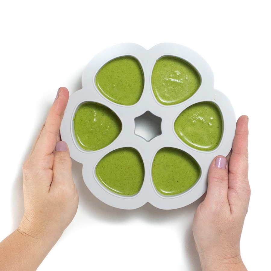 Hands holding a gray freezer storage tray with broccoli puree.
