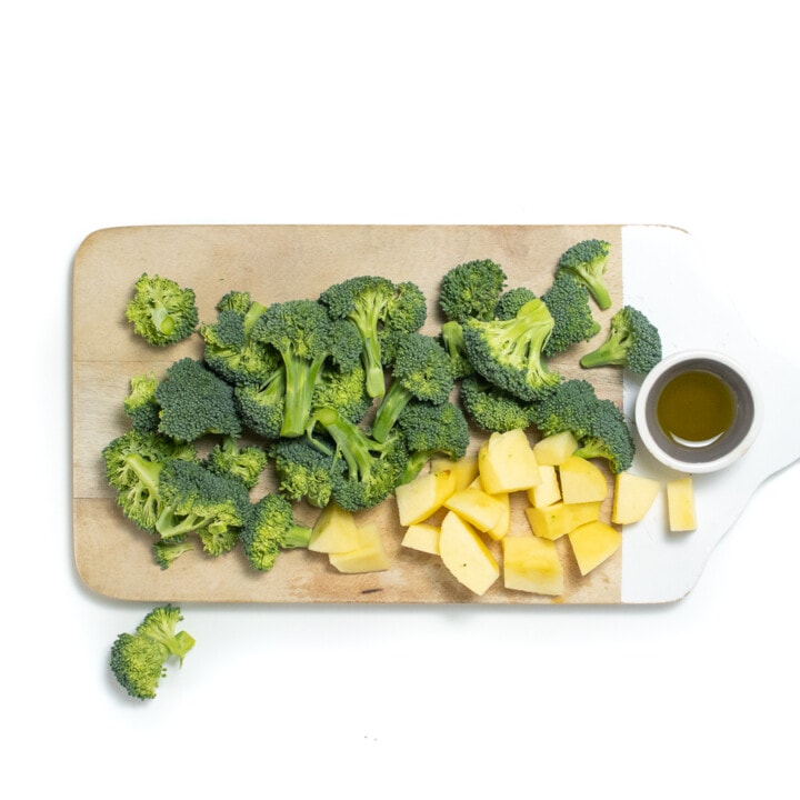 Cutting Board with cut broccoli and apples with a small dish of olive oil.