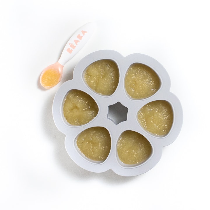 Gray baby food freezer tray filled with apple puree with a spoon sitting next to it. 