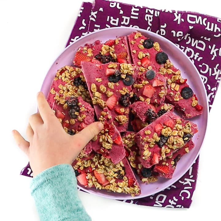 Girl reaching for a piece of berry granola bark. 