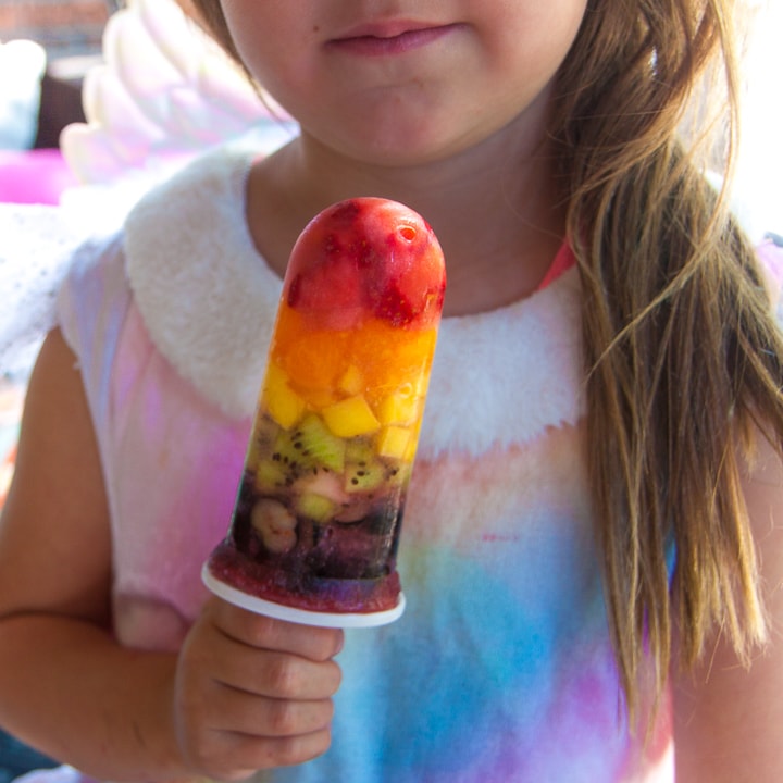 young girl holding a rainbow popsicle wearing a rainbow dress.