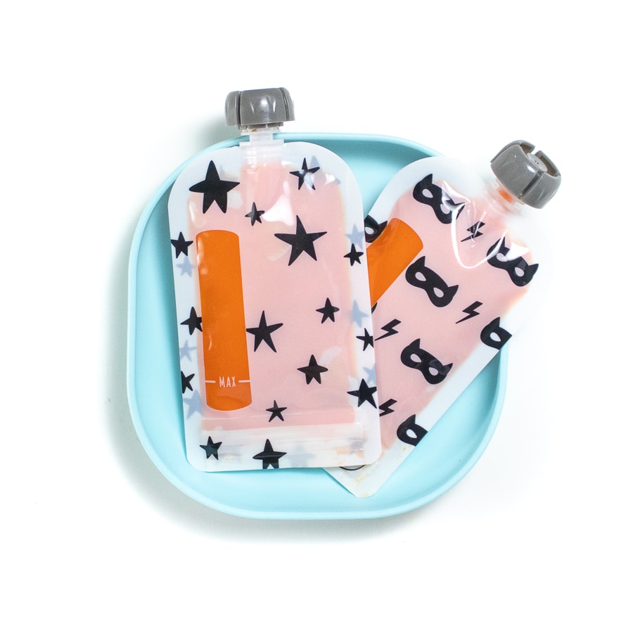 Blue plate with reusable black and white baby food pouches filled with orange carrot puree.