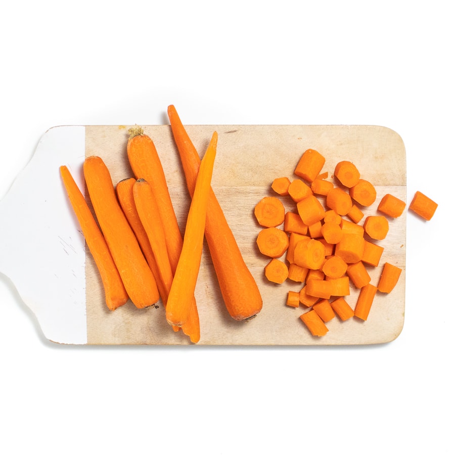 A wooden cutting board with a hole and sliced carrots.