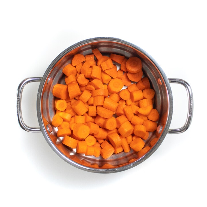A silver steamer basket with cooked sliced carrots.