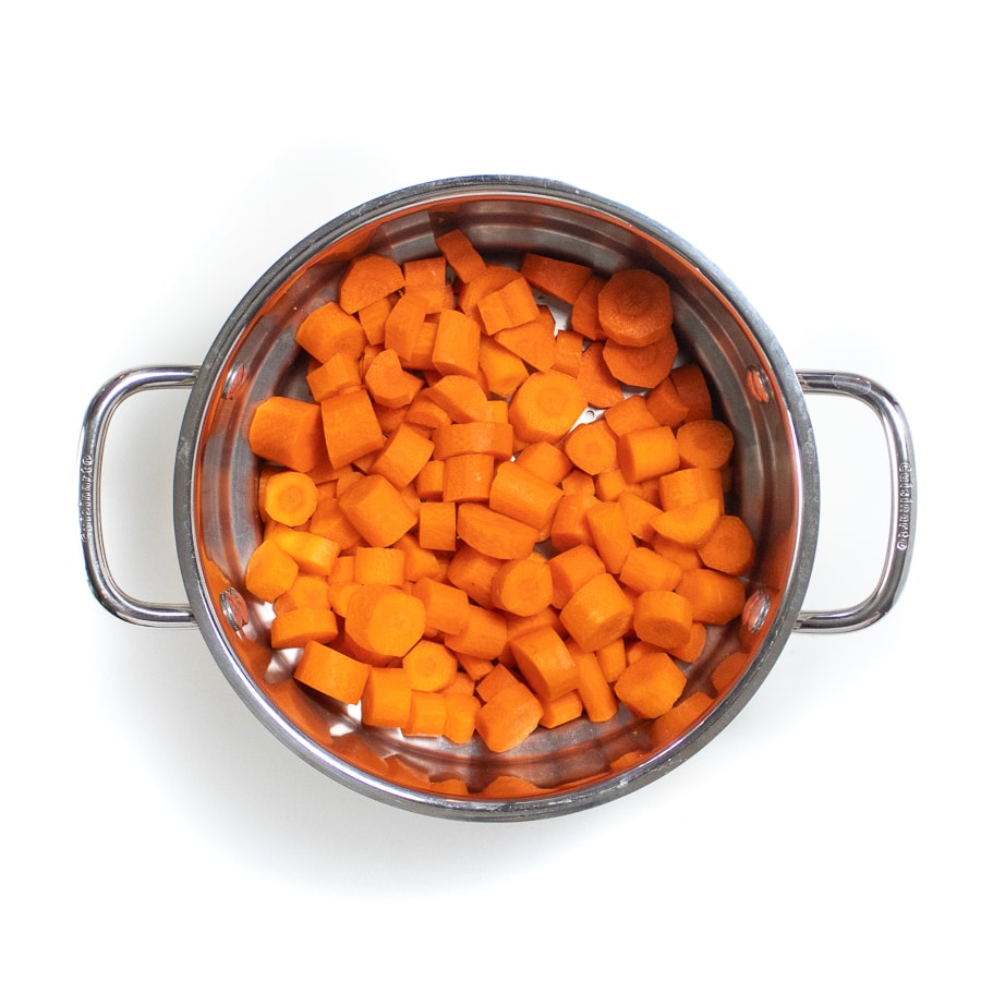 A silver steamer basket with cooked sliced carrots.