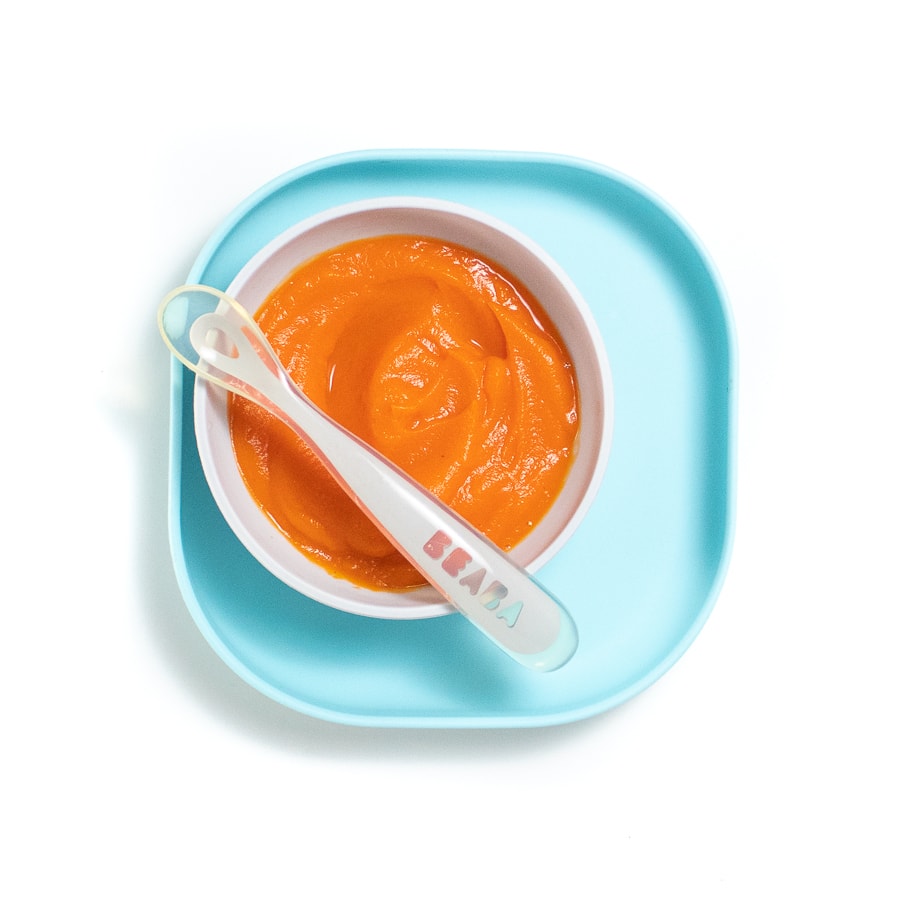 A blue baby plate with a gray baby bowl filled with a carrot purée with gray spoon resting on top.