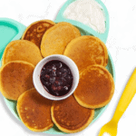 kids blue bear plate on a kitchen marble counter with a bunch of sweet potato pancakes on it with a berry sauce and yogurt.
