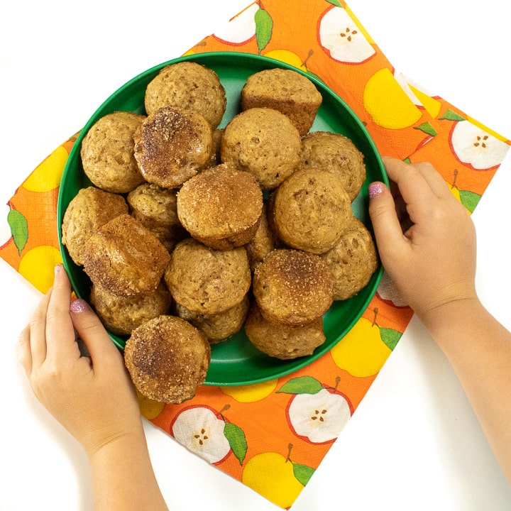 Small kids hand holding a plate of mini applesauce muffins.