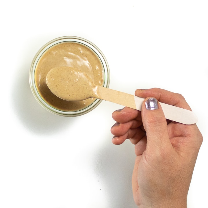 Hand with a spoon dipping into a jar of Carmel sauce.