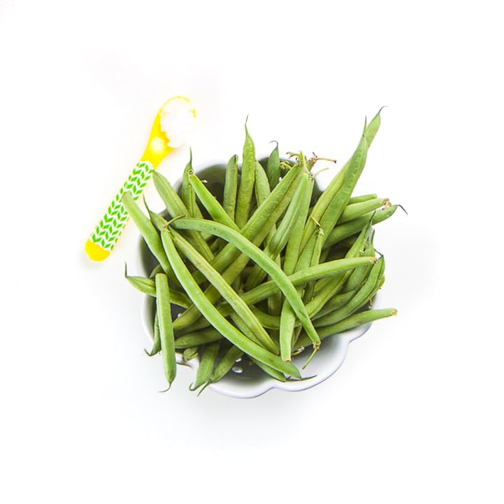 bowl full of green beans with a yellow spoon sitting next to it filled with coconut oil.