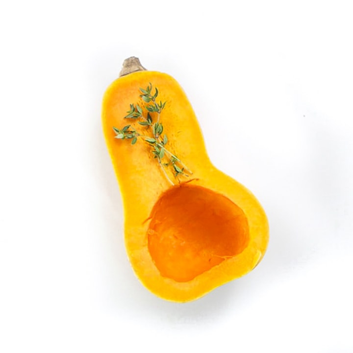 Butternut squash sliced open with thyme resting on it.