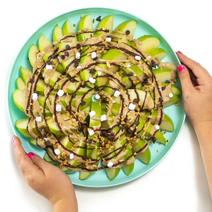 Kids hands holding the plate of healthy apple nachos for a snack or dessert.