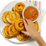 Small kids hand reaching for the pizza pinwheels on a plate.