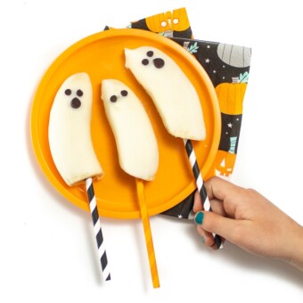Small kids hands reaching for a frozen banana in a ghost shape.