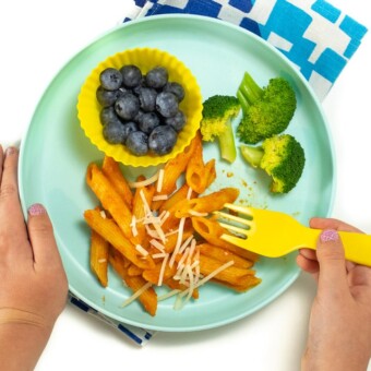 2 small kids hands holding a plate of pasta with hidden veggie sauce on it.