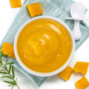 Butternut squash baby food puree in a small white bowl with baby spoon resting next to it.