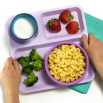 Hands holding a Purple school tray with instant pot Mac and cheese, broccoli and strawberries for a toddler or kid.
