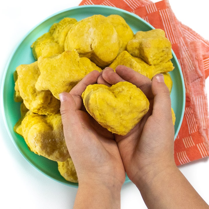 Small kid hands holding a heart shaped pumpkin biscuit.