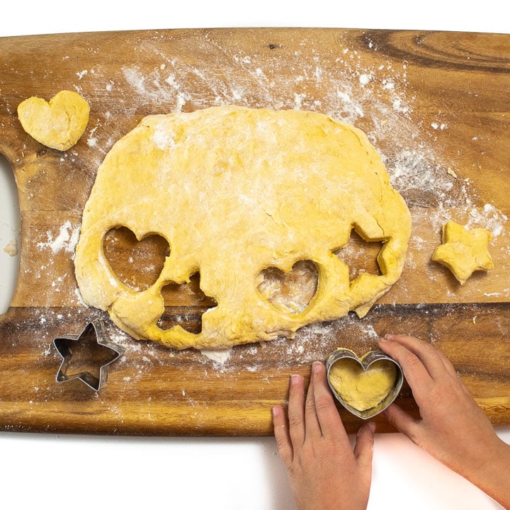 kid hands cutting out a heart shaped biscuit.