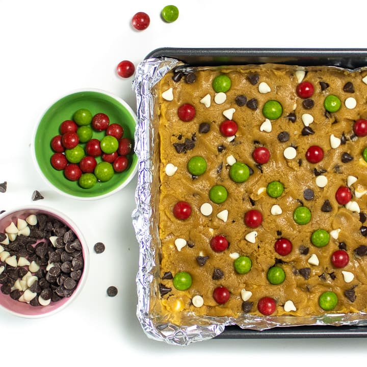 Christmas cookie bar dough with candy and chocolate chip toppings getting put on the top of it.