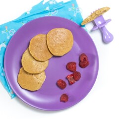 Purple plate with banana pancakes and raspberry pieces for baby.
