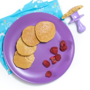 Purple plate with banana pancakes and raspberry pieces for baby.