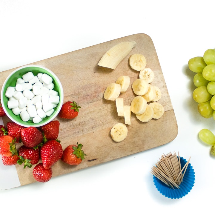 Cutting board with strawberries and cut bananas.