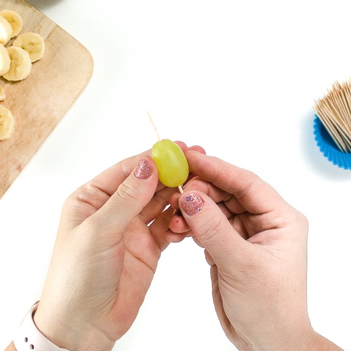 Hands holding the grapes on a toothpick.
