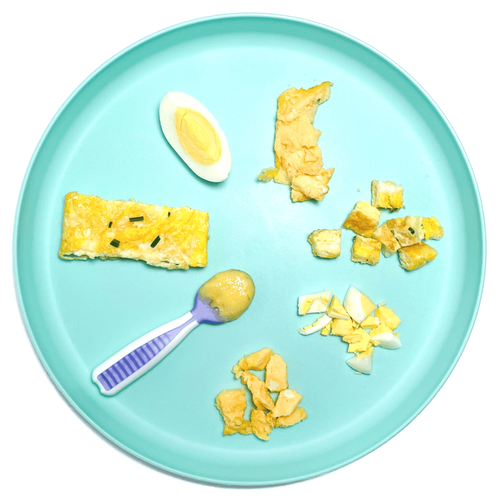 Blue baby plate with eggs cooked and cut in different ways to show the variety on how to serve eggs to baby. The plate is sitting on a white countertop.