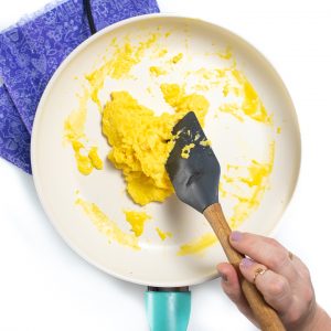 Adult hand making scrambled eggs.