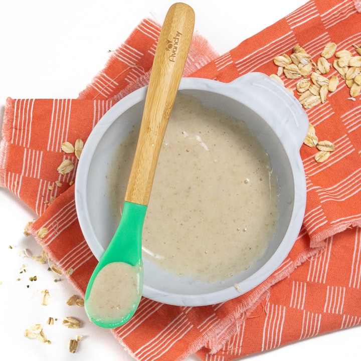 Bowl of oatmeal for baby with spoon resting on top of gray bowl.