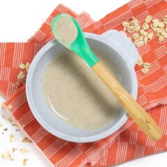 Gray baby bowl filled with oatmeal for babies with green spoon resting on top.