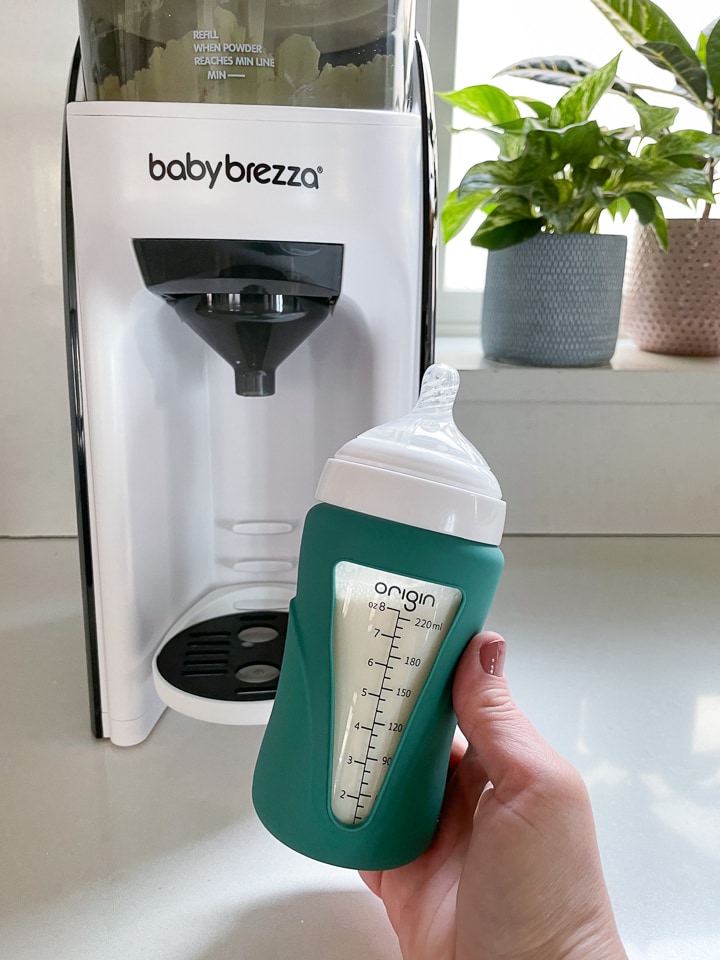 Hand holding bottle in front of a baby Brezza machine. 
