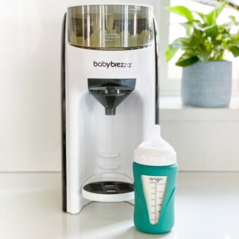 Glass bottle sitting in front of a baby Brezza advanced formula pro machine.