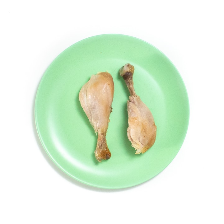 Green baby plate with two chicken drumsticks on it.